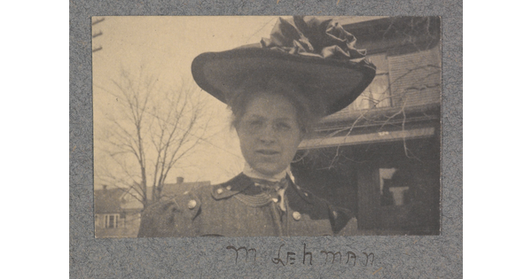 A black-and-white photograph of a White woman from the shoulders up, wearing a large brimmed hat with ruffles on top.