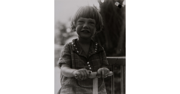 A black-and-white photograph of a young White child with short hair holding the handle of a toy of some sort.