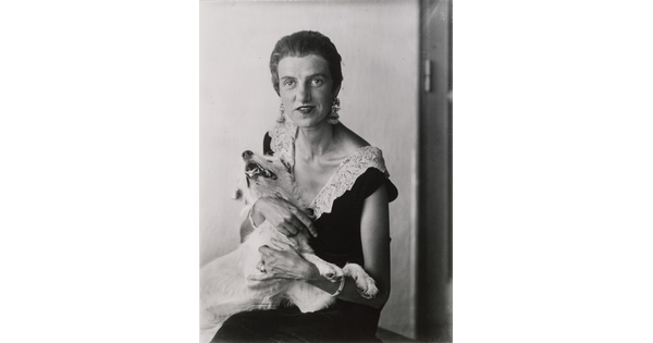 A black-and-white portrait photograph of a seated, nicely dressed White woman embracing a white dog.