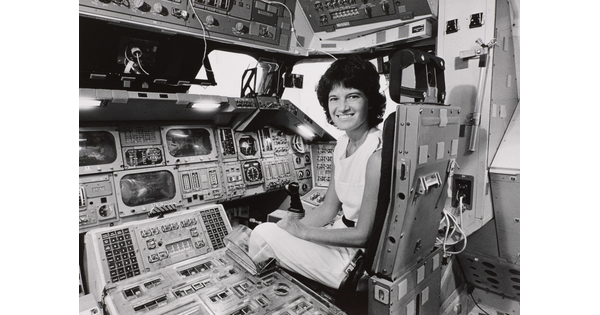 A black-and-white photograph of a White woman with short dark hair sitting in the cockpit of a space shuttle.