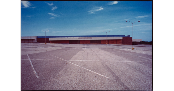 A color photograph of an abandoned strip mall and empty parking lot.