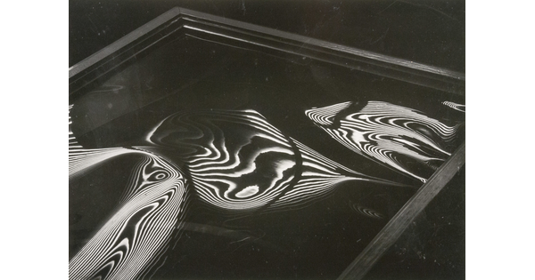 An abstract black-and-white photograph of a square-edged frame containing liquid-like organic round shapes with high-contrast nested contour lines.