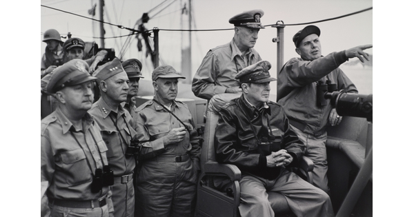 A black-and-white photograph of White men in military uniforms, binoculars hanging around their necks, looking in the direction one of the men is pointing.
