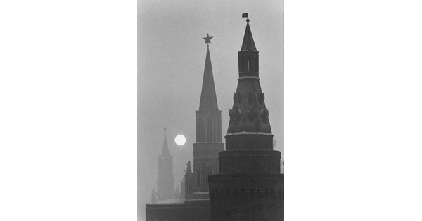 A black-and-white photograph of three spires fading into the distance with a bright, full moon rising.
