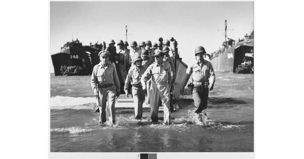A black-and-white photograph of a large group of men in military uniforms, most wearing helmets, exiting boats and wading onto a shoreline.