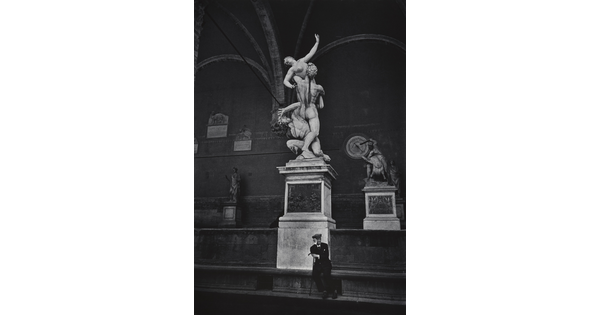 A black-and-white photograph of a man in a suit sitting below the statue of The Rape of a Sabine Woman in Florence, Italy.