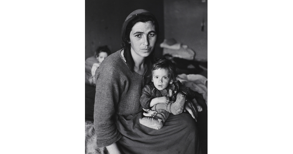A black-and-white photograph of a tired-looking White woman hunched over a small child in her lap.