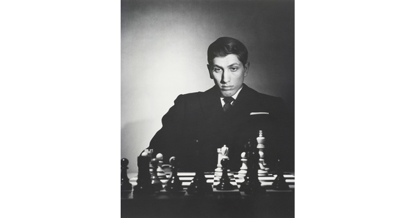 A black-and-white portrait photograph of a White man sitting and studying a chess board.