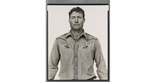 A black-and-white portrait photograph of a White man, with short hair and light facial hair, wearing a button-down shirt with Western details.