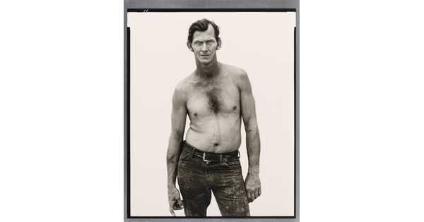 A black-and-white portrait photograph of a shirtless, White man with slicked back hair, wearing distressed jeans, and standing with one hip out.