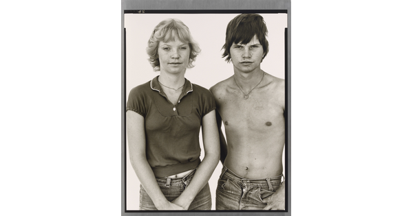A black-and-white portrait photograph of a young White woman with short blonde hair and a shirtless, young White man with short tousled hair.