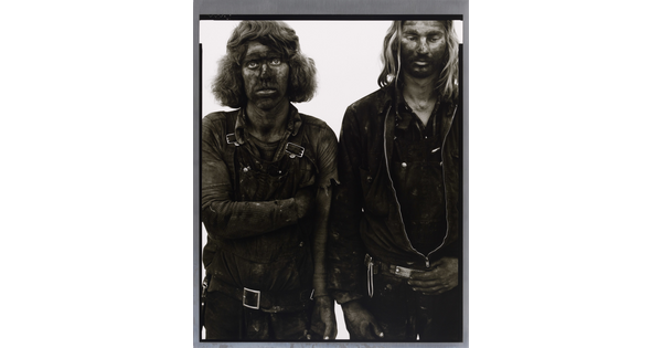 A black-and-white portrait photograph of two men standing side by side, both covered in dark coal dust.