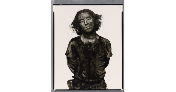 A black-and-white portrait photograph of a young man with curly hair covered in dark coal dust.