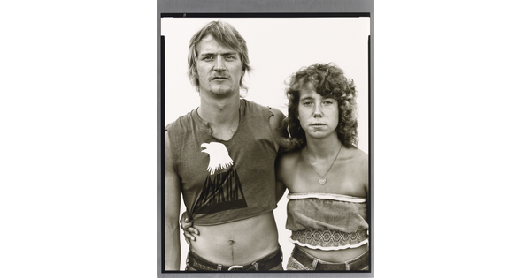 A black-and-white portrait photograph of a young White man and woman, arms around each other, both wearing crop-top shirts.