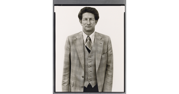 A black-and-white portrait photograph of a dark-haired, White man wearing a three-piece plaid suit with a tie.