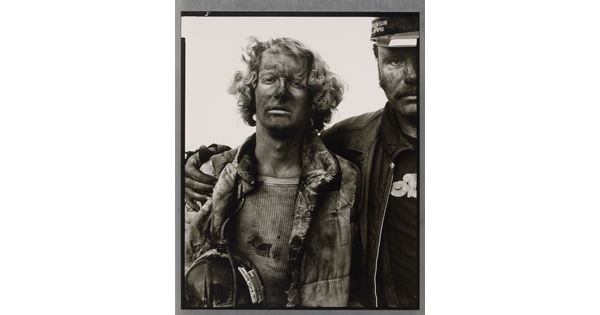 A black-and-white portrait photograph of two men, one with his arm around the other, both covered in coal dust and wearing dirty clothes.