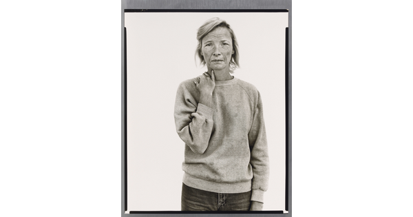 A black-and-white portrait photograph of a tired-looking White woman wearing a sweatshirt and holding her hand on her shoulder as if it might ache.