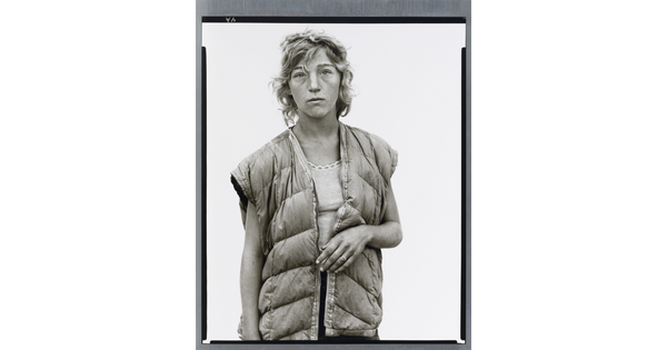 A black-and-white portrait photograph of a young White woman with short wavy hair wearing a puffer vest looking straight at the viewer.