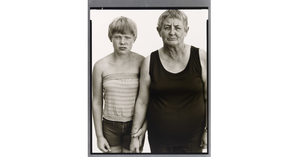 A black-and-white portrait photograph of a young White girl with short blonde hair wearing a tube top, and an older White woman with short gray hair wearing a black tank top.