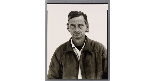 A black-and-white portrait photograph of a White man with a salt-and-pepper goatee wearing a collared shirt under a quilted jacket.
