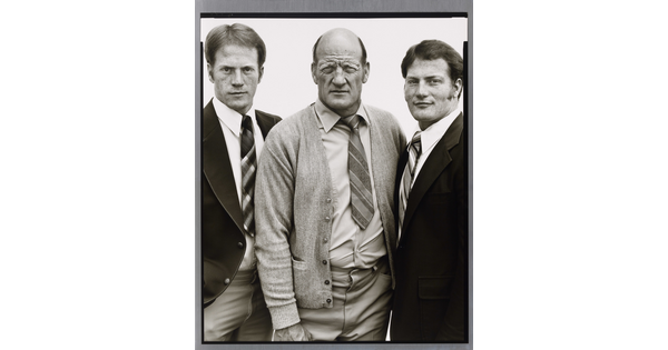 A black-and-white portrait photograph of three White men, two younger on the left and right and the one in the center middle-aged and bald, all wearing suits and ties.