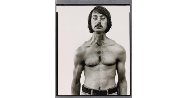 A black-and-white portrait photograph of a shirtless White man, with dark hair and a mustache, and thin but with muscled shoulders and arms.