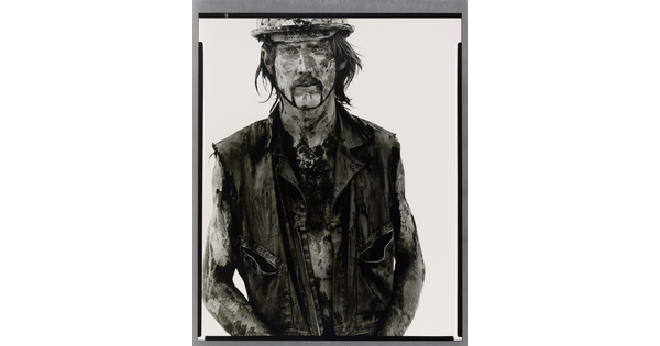 A black-and-white portrait photograph of a White man covered in dirt and oil wearing a vest and hard hat.