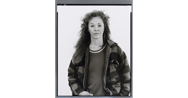 A black-and-white portrait photograph of a middle-aged White woman with long hair wearing a checked jacket.