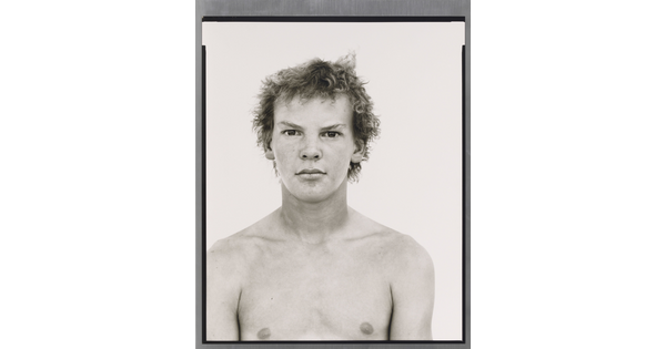 A black-and-white portrait photograph of a shirtless White teenage boy with messy hair.