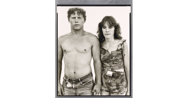 A black-and-white portrait photograph of a young, shirtless White man holding hands with a young White woman wearing a tank top and shorts.