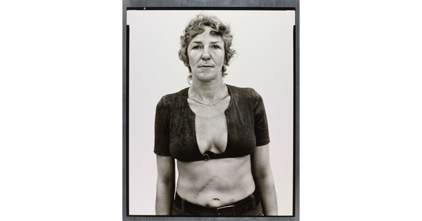 A black-and-white portrait photograph of a White woman with short, curly hair wearing a cropped shirt with a very low neckline.