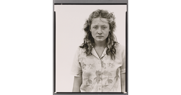 A black-and-white portrait photograph of a White teenage girl with her blonde hair pulled back in barrettes and wearing a floral button-up blouse.