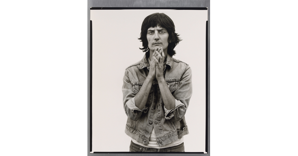 A black-and-white portrait photograph of a light-skinned woman wearing a denim jacket and holding her hands together up to her chin.