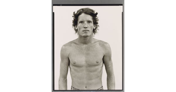 A black-and-white portrait photograph of a shirtless young White man with freckles across his face and shoulders.