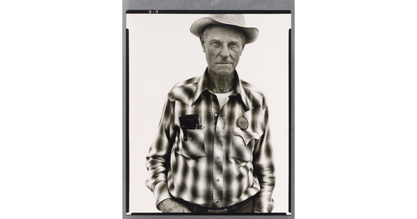 A black-and-white portrait photograph of an older White man wearing a plaid, button-down shirt and western hat.