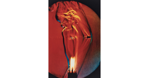 A color photograph of a lit candle with a bullet going through the flame.