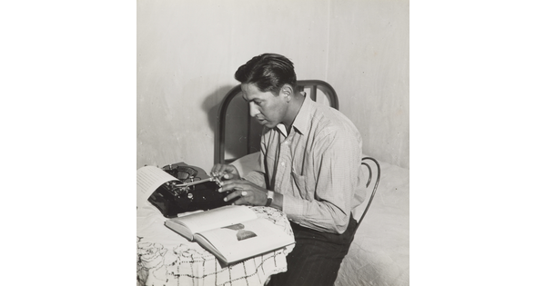 A black-and-white photograph of a Native American man typing on a typewriter.