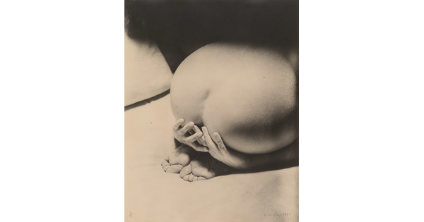 A black-and-white photograph of a White person from behind showing a bare bottom and back, feet tucked under, and hands partially covering their behind.