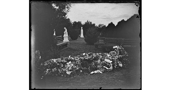 A black-and-white image of a cemetery with a grave completely covered in fresh flowers in the foreground.