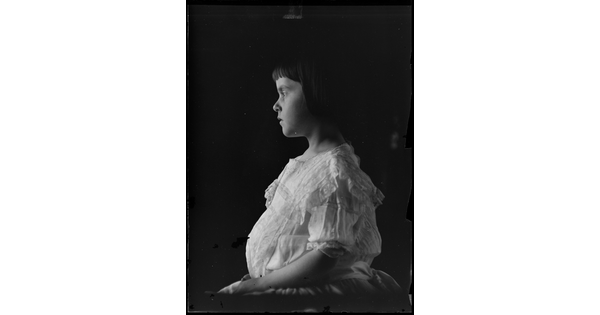 A black-and-white image of a young White girl in profile wearing a white dress.