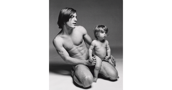 A black-and-white photograph of a nude White man kneeling and holding a nude White toddler on his knee.