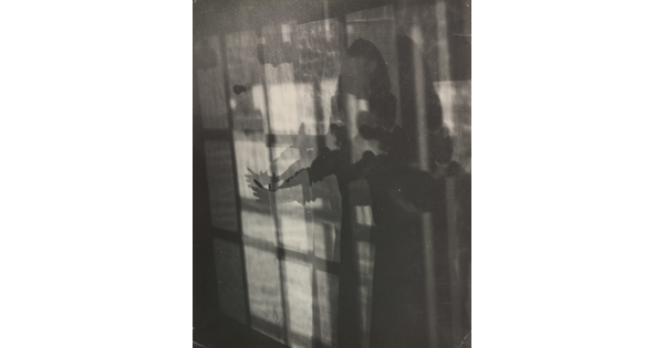 An abstract black-and-white photograph showing a human figure extending their arm in abstracted layers of shadow and light.