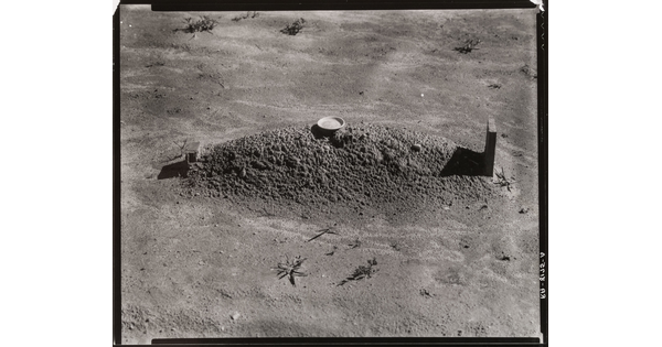 A black-and-white photograph of a freshly dug grave and headstone in a barren landscape.