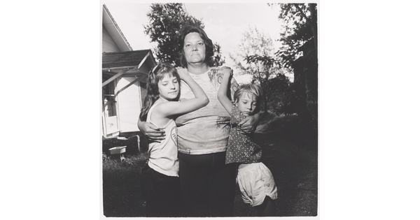 A black-and-white photograph of a middle-aged White woman with her arms around two young children who are hanging on her shoulders.
