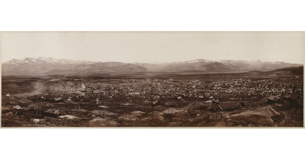 A black-and-white panoramic landscape photograph of a city with a mountain range in the background.