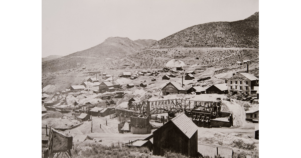A black-and-white photograph of a mining town at the base of mountains.