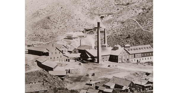 A black-and-white photograph of industrial buildings with smoke stacks in a rocky valley.