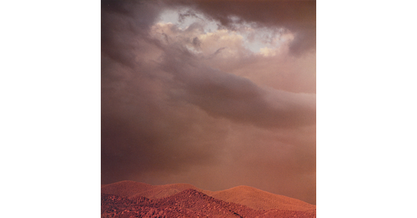 A color photograph of reddish mountain tops under dark, heavy clouds.