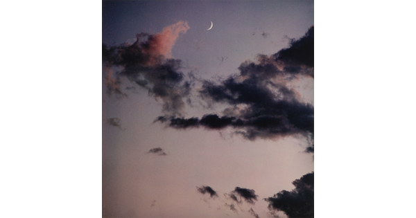 A color photograph of a blue-gray sky, dark clouds, and a crescent moon.