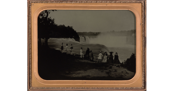 A black-and-white photograph in a gold frame of a group of men and women on a cliff overlooking a large waterfall.